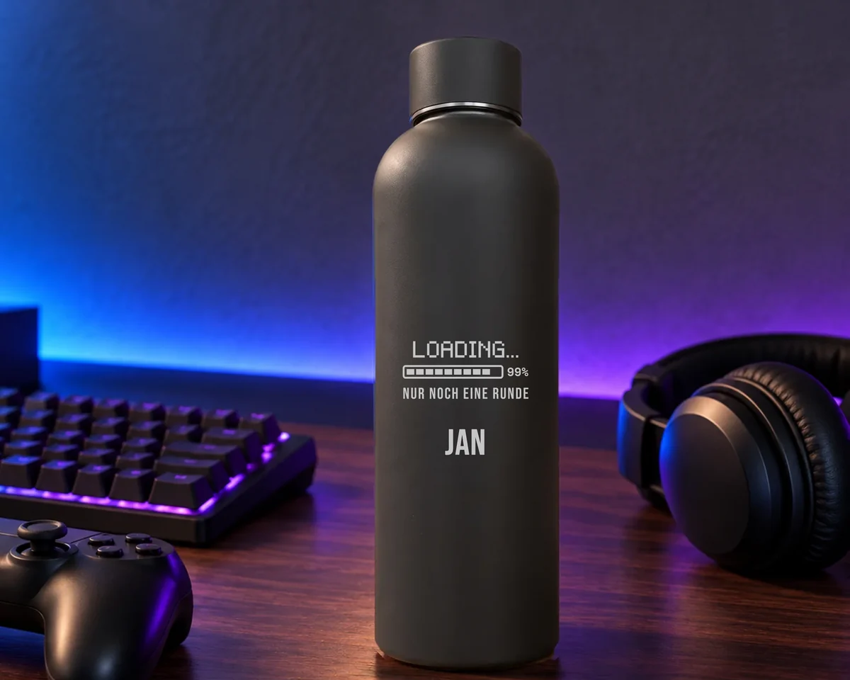 Schwarze Thermosflasche mit gravierten Ladebalken «Loading 99 %, nur noch eine Runde» und dem Namen Jan auf einem Gaming-Schreibtisch mit beleuchteter Tastatur, Controller und Kopfhörern