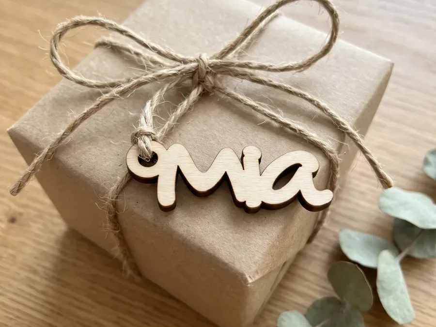 Geschenkanhänger aus Holz mit dem Namen Mia, mit Juteschnur an einem Päckli in Packpapier gebunden, daneben Eukalyptus