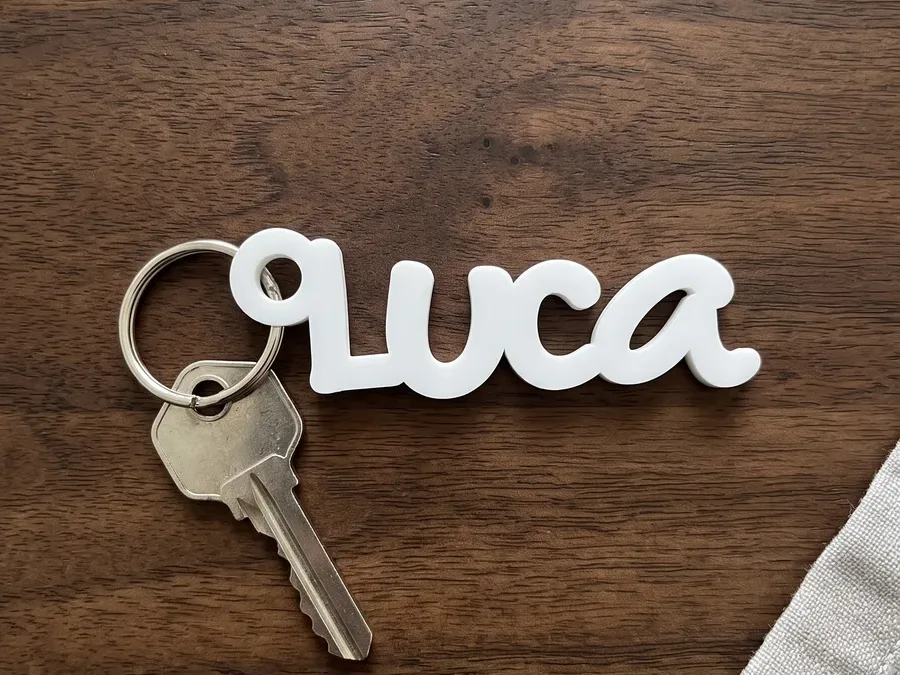 Schlüsselanhänger aus weissem Acryl mit dem Namen Luca, die Buchstaben hängen zusammen, auf einem dunklen Holztisch