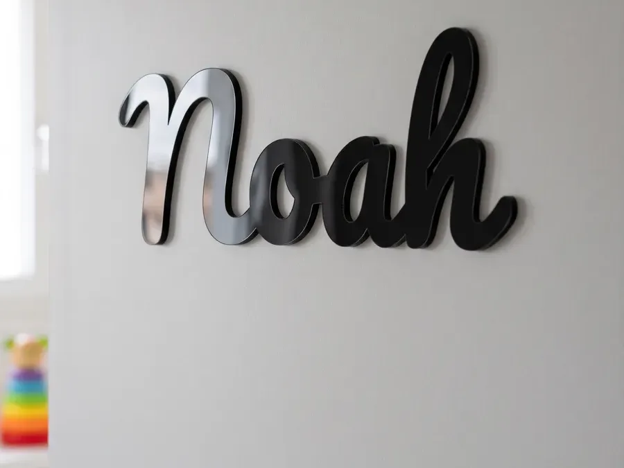 Namensschild aus schwarzem Acryl mit dem Namen Noah in Schreibschrift an einer hellgrauen Tür neben der Türklinke