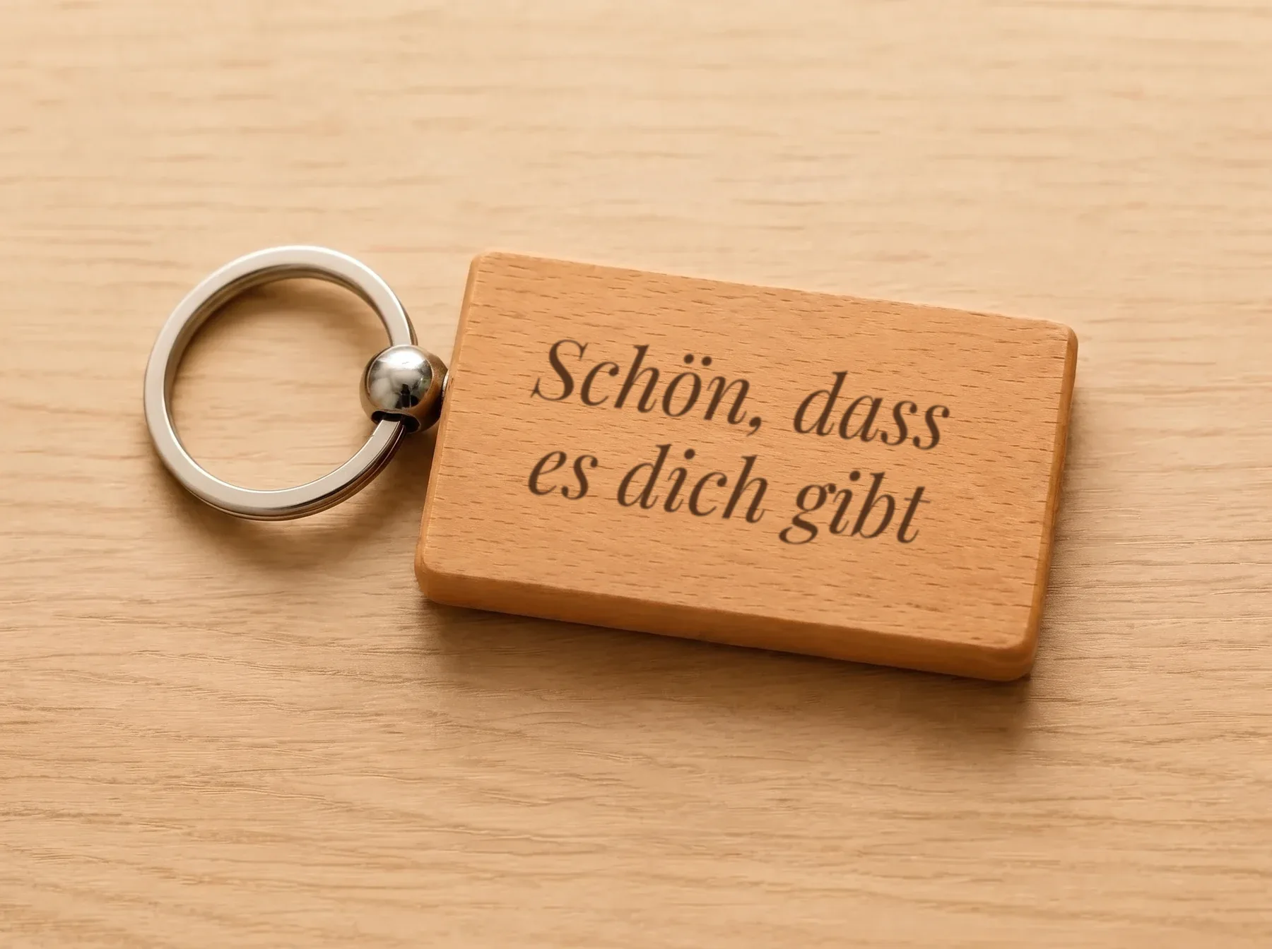 Holzanhänger mit Schlüsselring auf einem hellen Holztisch, graviert mit dem Spruch Schön, dass es dich gibt in Schreibschrift