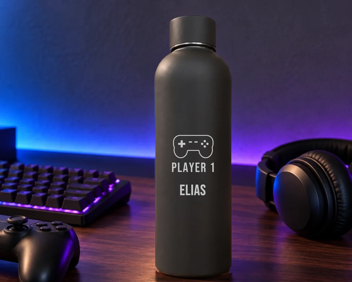 Mattschwarze Thermosflasche mit Gamepad-Motiv, dem Schriftzug Player 1 und dem Namen Elias, auf einem Schreibtisch neben beleuchteter Tastatur, Controller und Kopfhörer