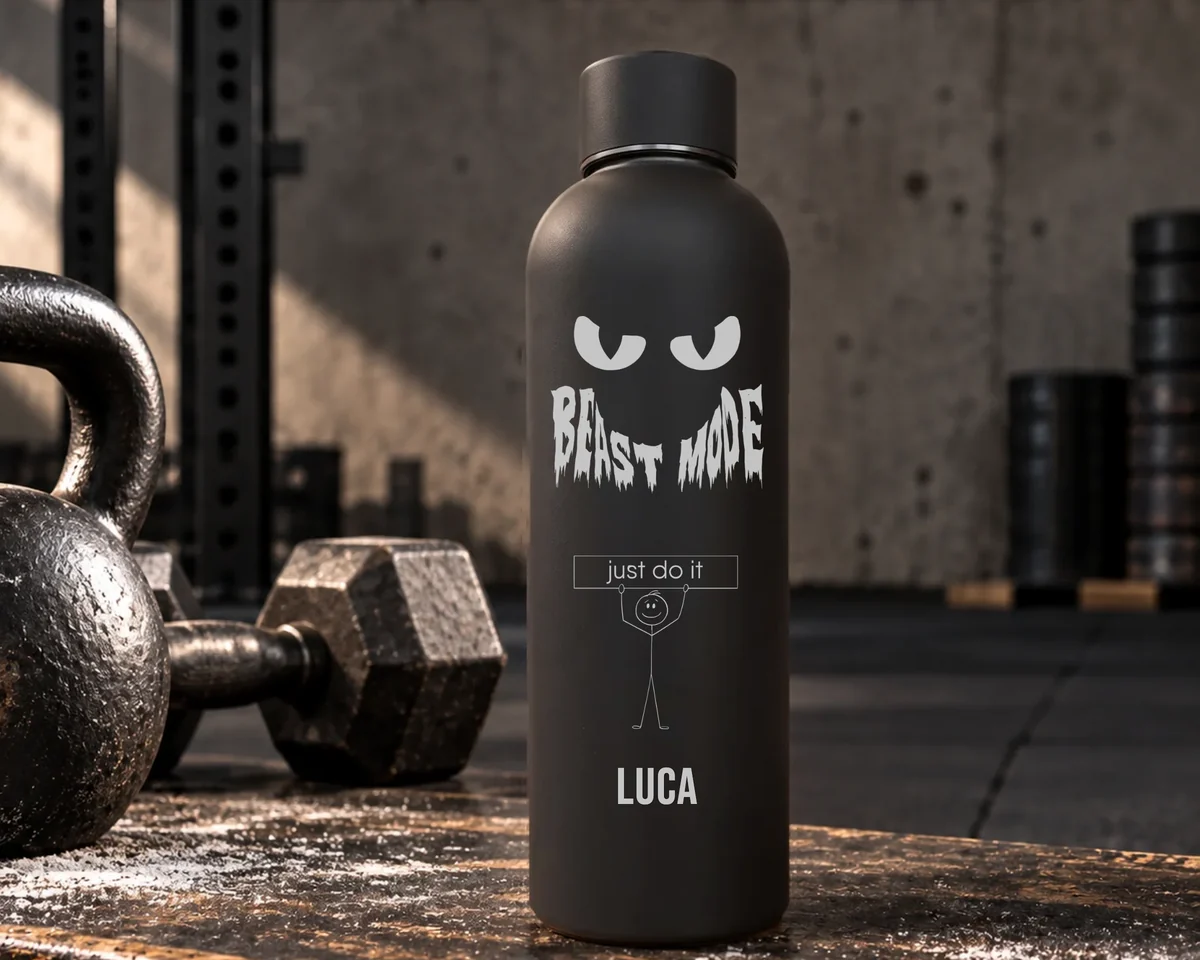 Mattschwarze Thermosflasche mit der Gravur Beast Mode, einem Strichmännchen mit Schild just do it und dem Namen Luca, in einem Fitnessraum neben Kettlebell und Kurzhantel