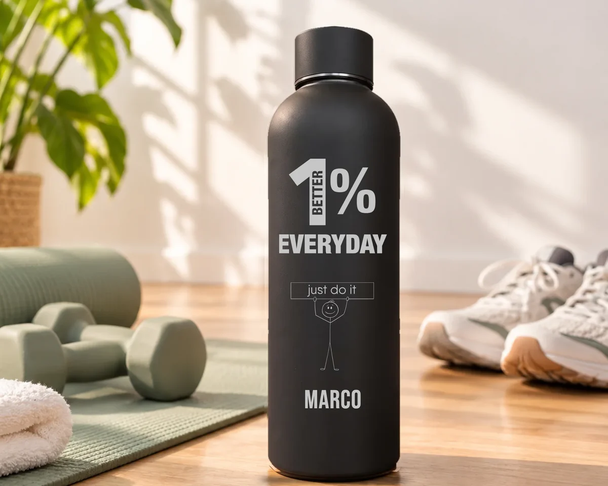 Mattschwarze Thermosflasche mit der Gravur 1% Better Everyday, einem Strichmännchen mit Schild just do it und dem Namen Marco, auf einem Holzboden neben Yogamatte, Hanteln und Turnschuhen
