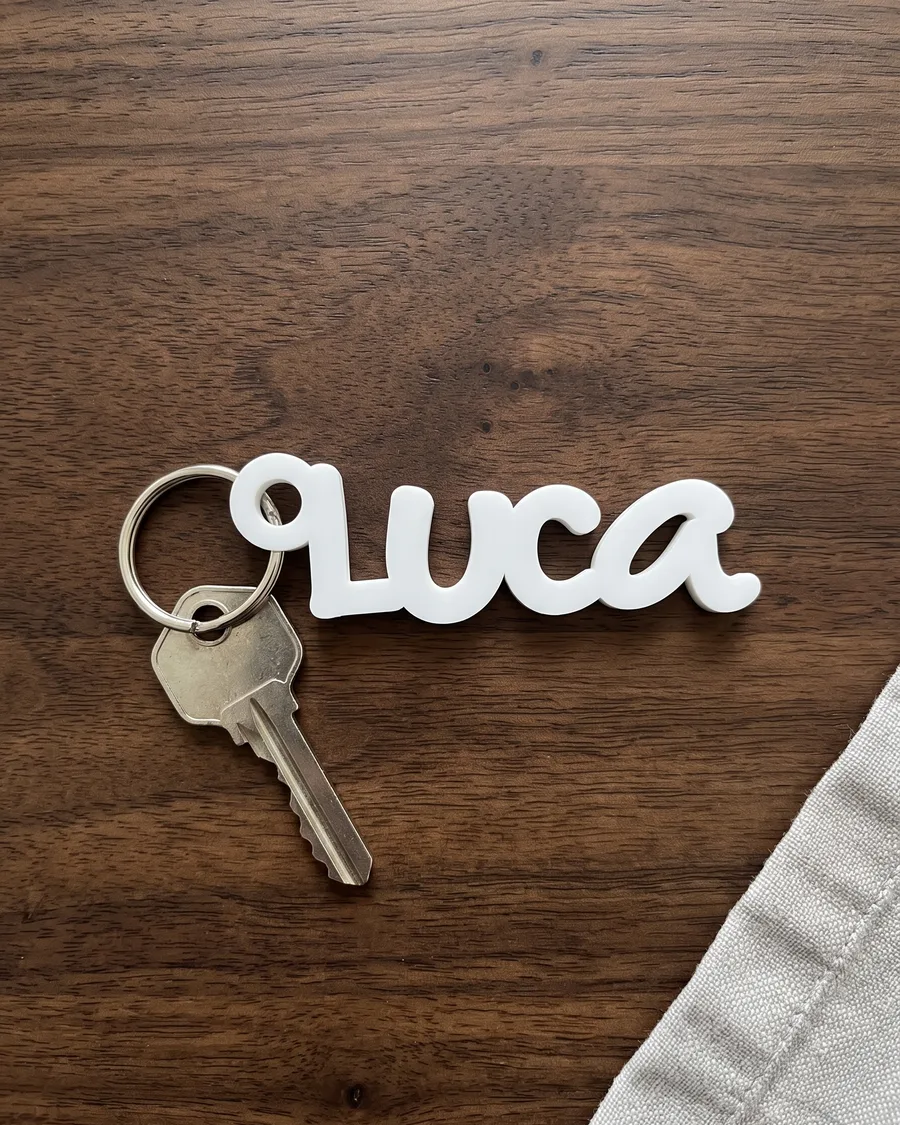 Schlüsselanhänger aus weissem Acryl mit dem Namen Luca auf einem dunklen Holztisch