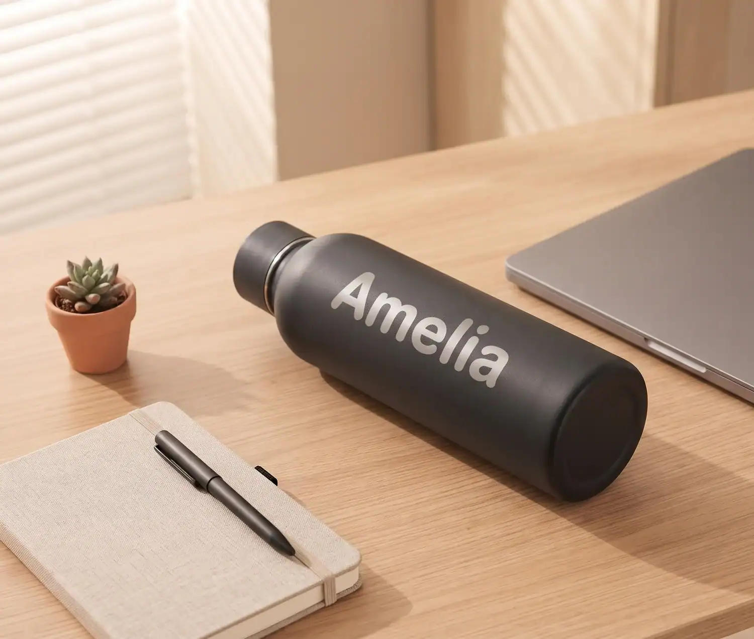 Thermosflasche mit dem gravierten Namen Amelia auf einem Schreibtisch neben Laptop und Notizbuch
