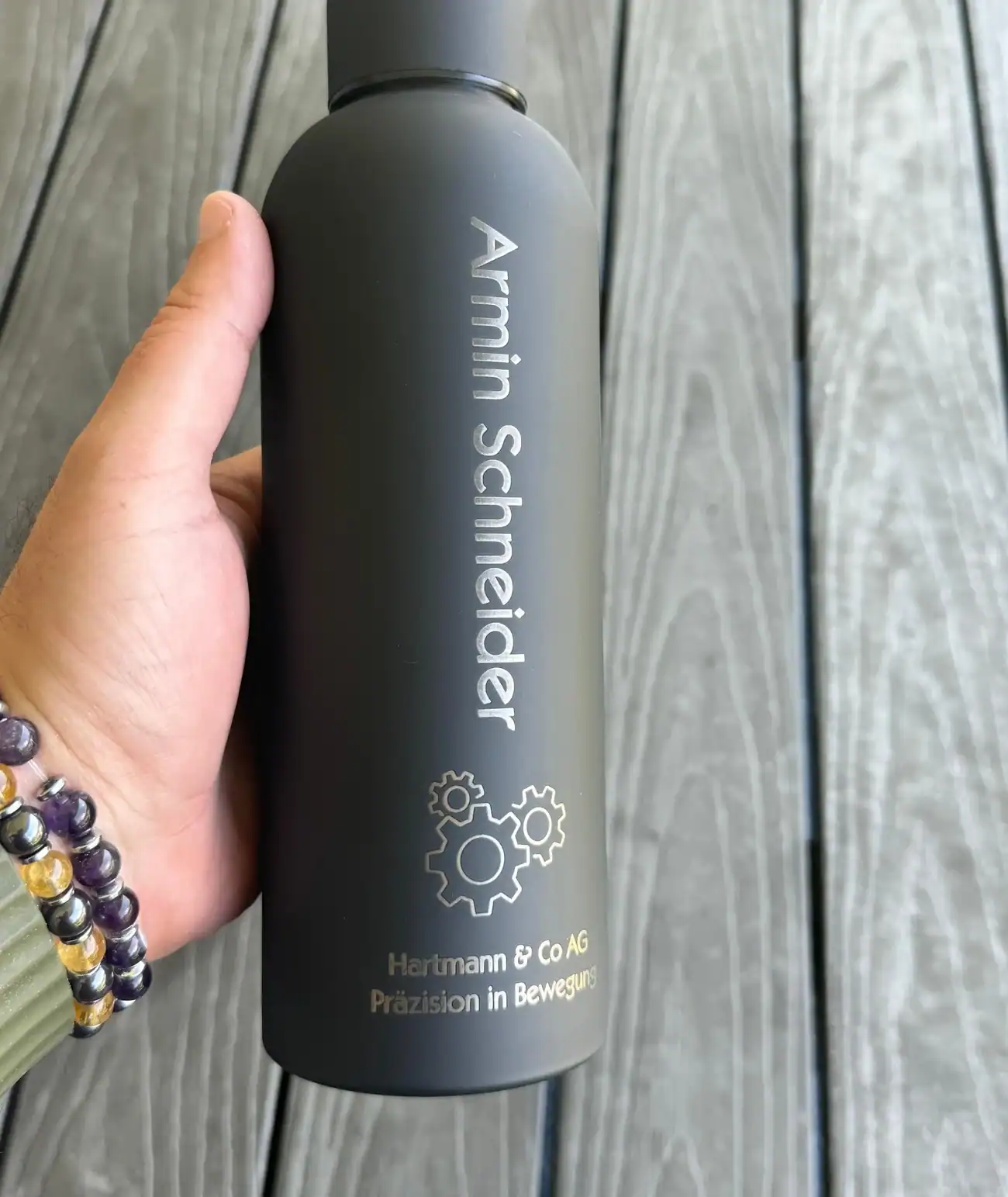 Eine Hand hält die echte mattschwarze Thermosflasche mit graviertem Namen und Logo